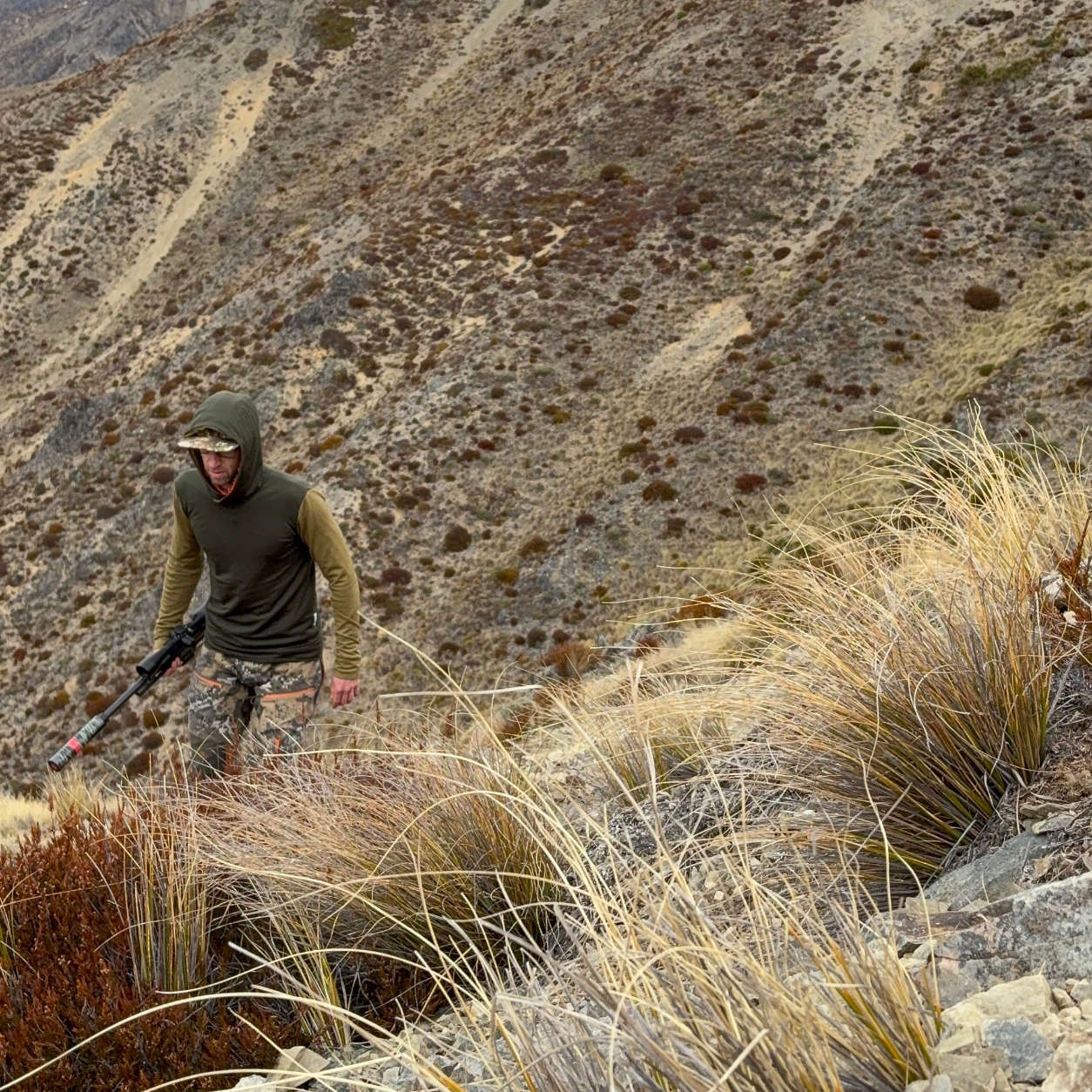 Hunter in the men’s Beech Green and Tussock Rangitata hoodie hiking up an alpine hillside.